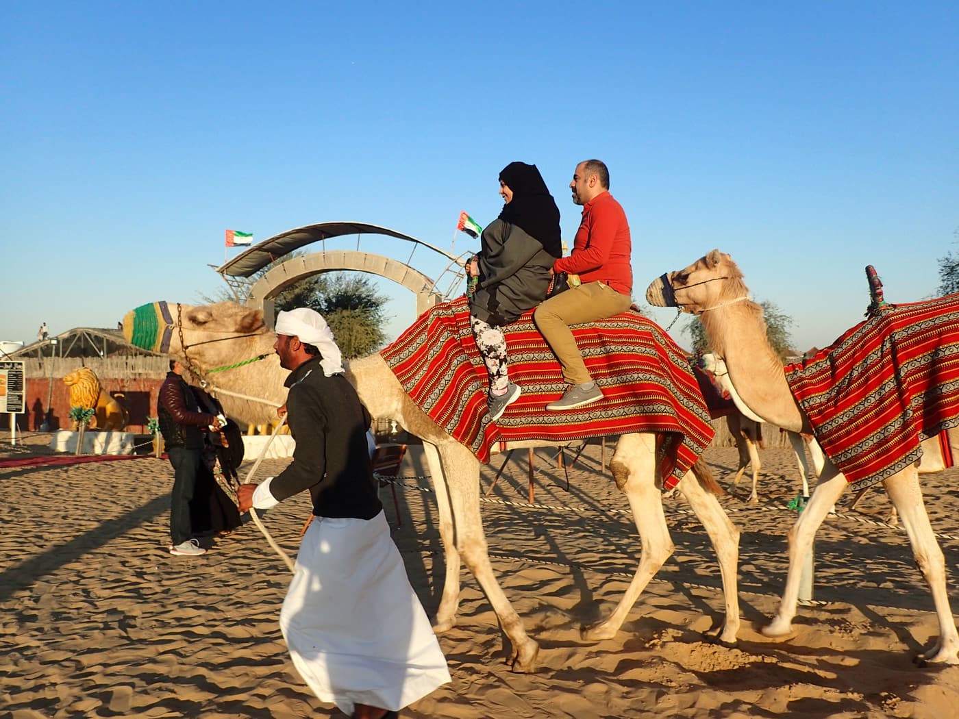 Visitors riding camels led by a handler at a desert camp