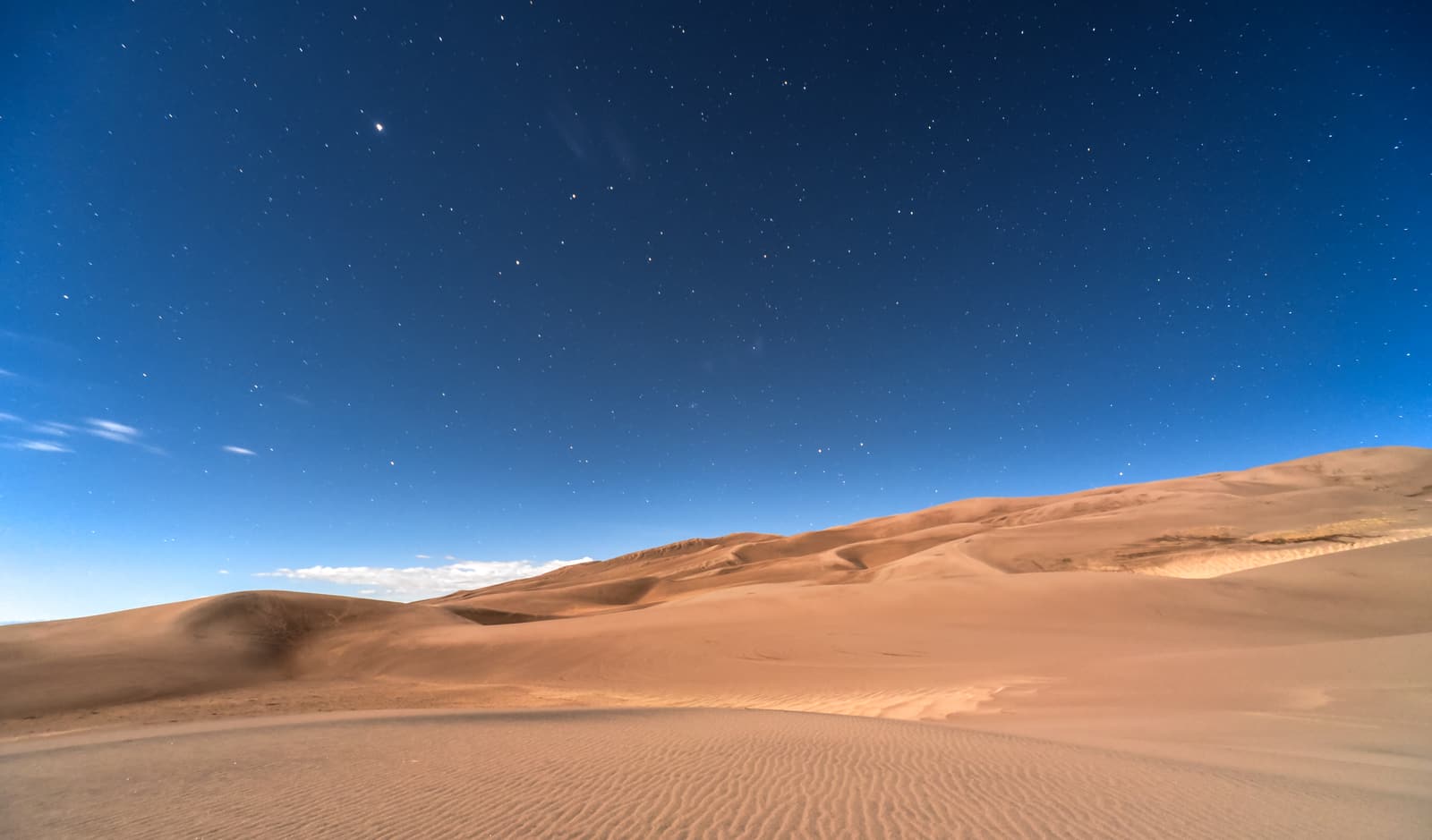 A starry night sky over desert dunes