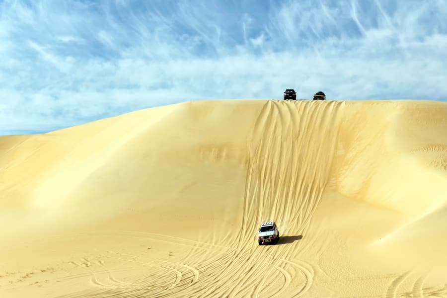 4x4s driving down the face of a tall dune